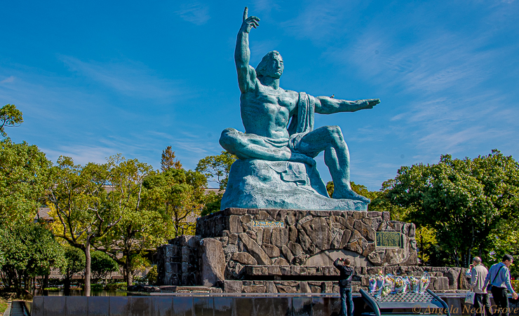 This is the ten foot high Peace Statue created by Seibo Kitamura for the Nagasaki Peace Park. The right hand points to the threat of nuclear weapons, the left hand symbolizes eternal peace. The mild face, symbolizing divine grace, has eyes gently closed in prayer for the repose of the bomb victim's souls. The folded right leg signifies meditation and the left leg stands ready to help people of the world.
The statue is a mixture of Western and Eastern art, religion and ideology.PHOTO; ANGROVE